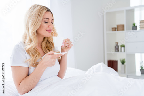 Photo of cheerful beautiful lady lying cozy linen quarantine time white sheets blanket amazing energetic morning good mood smell fresh hot coffee overjoyed stay home wear pajama indoors