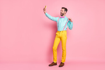 Canvas Print - Full length photo of handsome guy trend clothes browsing telephone recording video for blog post wear shirt suspenders bow tie yellow trousers shoes isolated pastel pink color background