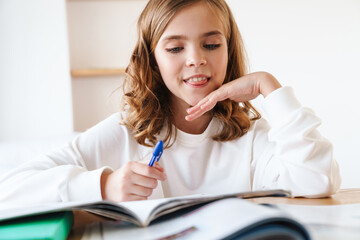 Wall Mural - Photo of happy girl writing in exercise book while doing homework