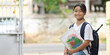 © Prathankarnpap - A schoolgirl is holding painting equipment and carrying a school bag while standing and waiting for a school bus.