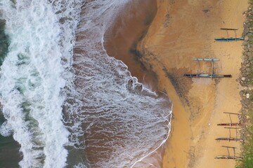 aerial drone bird view shot of the sea shore with turquoise water, an empty yellow sand beach with fishing long boats, white waves and foam forming beautiful textures, patterns, shapes. Sri Lanka