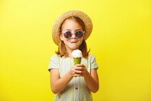Beautiful Little Girl Holding An Ice Cream And Going To Eat It, Licking Her Lips, Dressed In A Summer Dress, Straw Hat And Sunglasses, Standing On Yellow Isolated.