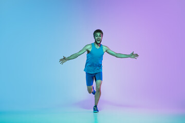 The first. Portrait of young caucasian man running, jogging on gradient studio background in neon light. Professional sportsman training in action and motion. Sport, wellness, activity, vitality