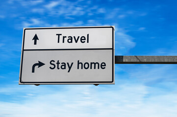 Travel versus stay home. Travel and stay at home concept. White two street signs with arrow on metal pole. Directional road. Crossroads Road Sign, Two Arrow. Blue sky background.