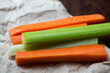 close up filled frame shot of party snack food. A bunch of crunchy orange carrot and juicy green celery sticks laying on a piece of brown paper on a dark brown wooden table
