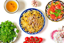National Uzbek Pilaf With Meat, Achichuk Salad Of Tomato, Cucumber, Onion In Plate With Traditional Pattern, Cilantro, Cherry Tomatoes, Garlicbread Tortilla - Patir On White Wooden Table Top View
