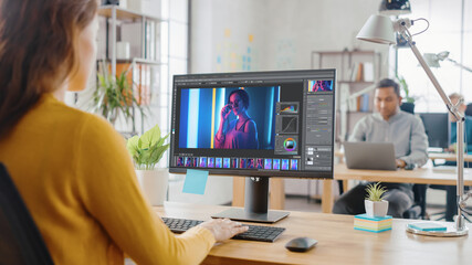 Poster - Over the Shoulder: Creative Young Woman Digital Editor Works in Photo Editing Software on Her Personal Computer with Big Display. In the Background Loft Office with Diverse Team of Young Professionals