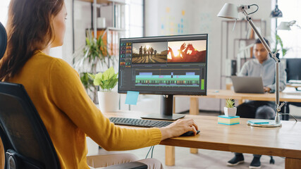 Poster - Over the Shoulder: Creative Young Woman Works with Footage on Her Personal Computer with Big Display. In the Background Bright Office where Diverse Team of Young Professionals Work.
