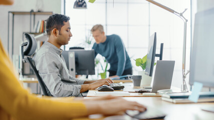 Poster - Man Working on Computer. In Foreground Anonymous Young Woman Sitting at Her Desk Using Computer Keyboard. In the Background Bright Office where Diverse Team of Young Professionals Work.