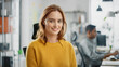 © Gorodenkoff - Portrait of Beautiful Young Woman with Red Hair Wearing Yellow Sweater Smiling at Camera Charmingly. Successful Woman Working in Bright Diverse Office.