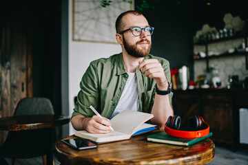 Handsome creative author sitting at cafe interior with notebook