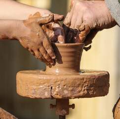 Hands of a boy and a man sculpt clay dishes.