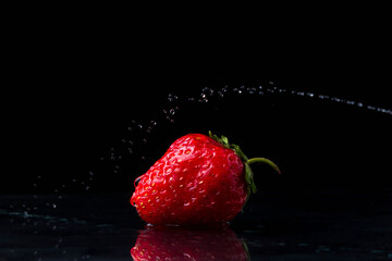 Strawberries on a black background. Creative photo of strawberries. A stream of water is above the strawberries. Water sticks over strawberries. 