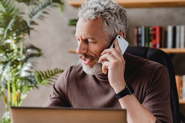 senior man talking on mobile phone while sitting in office at the desk