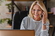 © InsideCreativeHouse - Smiling casual senior woman using laptop while talking on smartphone.