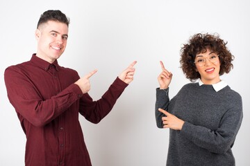 Wall Mural - Advertisement concept. Positive, pretty, caucasion woman with beaming smile in jeans shirt on grey background is pointing with her two index finger and looking on empty copy space.