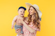 © Shopping King Louie - Happy young mother in a summer hat holding a little boy on a yellow background