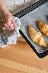 A woman is cooking croissants. Finished baking. Delicious traditional french crispy croissants for breakfast. Homemade bakery, cuisine for family. Girl chef work on kitchen table. Raw croissants