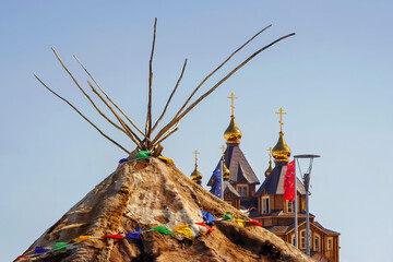 Yaranga (traditional home of the Chukchi - the indigenous people of Chukotka) against the background of the Christian Orthodox Cathedral. Tent made of deer skins and furs. Anadyr, Chukotka, Russia.