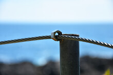 A Close Up Image Of A Wire Boundary Rope Welded To A Metal Pole To Create A Safety Boundary In A Wooded Area. 