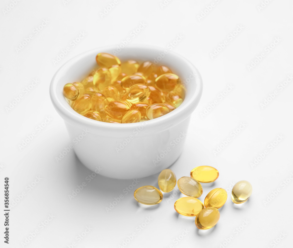 Bowl with fish oil capsules on white background