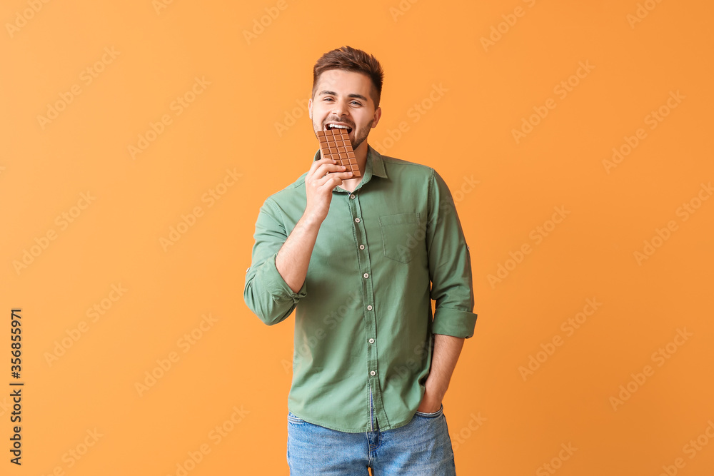 Handsome young man with tasty chocolate on color background