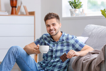 Wall Mural - Handsome young man with tasty chocolate and cup of tea at home