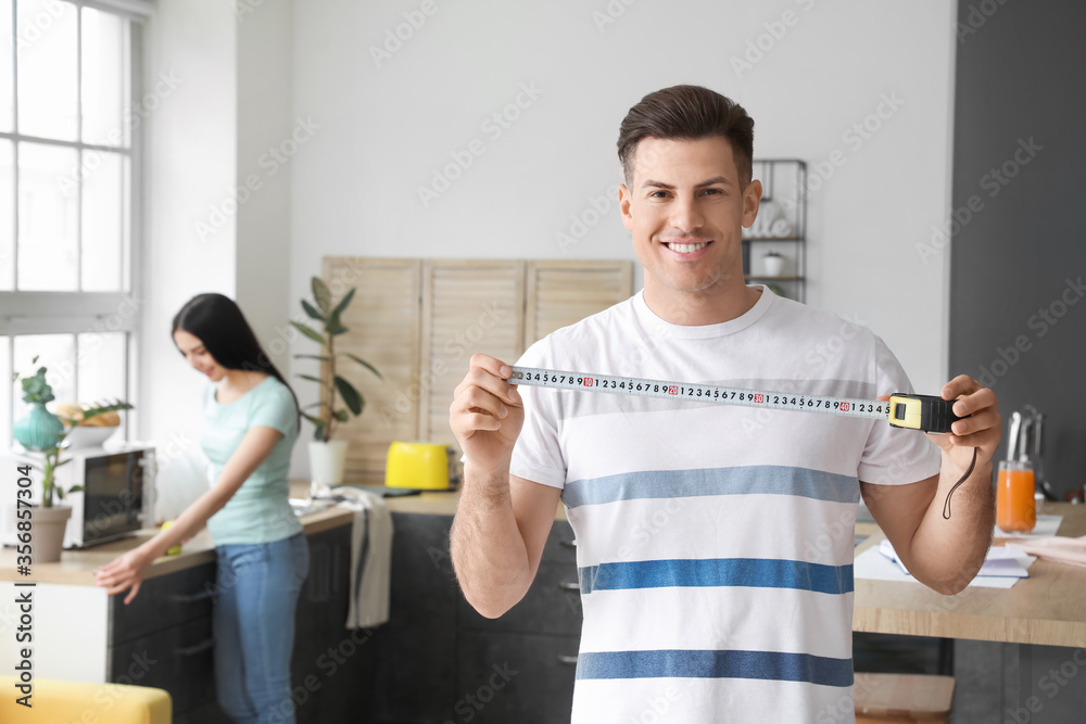 Young man with measuring tape in kitchen