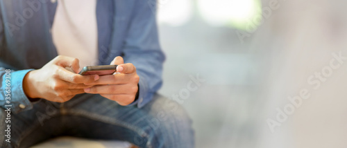 Fotografía A man using smartphone while sitting on sofa at hotel lobby with blurred backgro