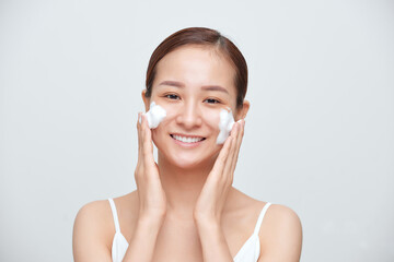 Wall Mural - Portrait of young Asian woman applying foaming cleanser against white background.