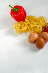 raw tagliatelle pasta with eggs, tomatoes and bell peppers on the table