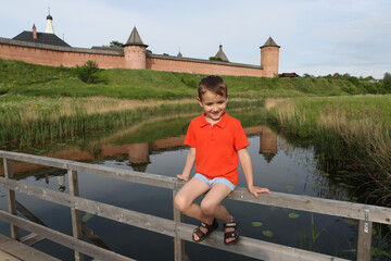 Wall Mural - Happy child in Suzdal town, Vladimir region, Russia. Active recreation in summer. Travel in Russia. National tourism. Kamenka river, Suzdal Kremlin, landmark. View, scenery