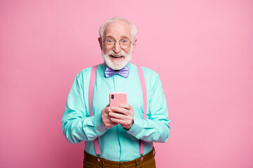 Sticker - Portrait of positive cheerful old man blogger use cellphone comment social media news repost share wear teal turquoise shirt purple violet bow tie isolated pastel pink color background