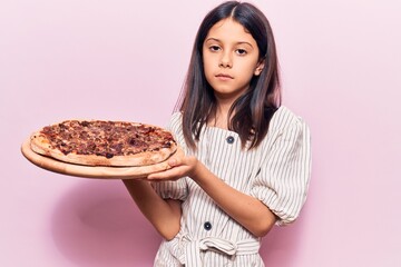 Poster - Beautiful child girl holding italian pizza thinking attitude and sober expression looking self confident