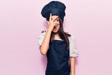 Sticker - Beautiful child girl wearing cooker uniform peeking in shock covering face and eyes with hand, looking through fingers afraid