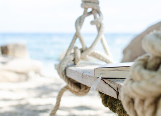 Closed book on beach swing with tropic ocean in background, holiday reads on Ko Tao island, Thailand