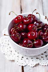 Wall Mural - Sweet ripe red cherry in white bowl on vintage napkin. Summer natural low calories dessert. Wooden background. Close up macro. Copy space for text