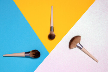 Three professional makeup brushes flat lay on a bright pink, yellow and blue background with copy space. Template for cosmetics product display montage or advertising text. Beauty and skincare concept