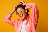 Fototapeta Tęcza - Debonair African woman with perfect smile , curly hairs and natural make up posing in pink trendy jacket on yellow background in studio.