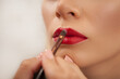 Unrecognizable makeup artist using red lipstick on the lips of a woman