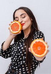 Canvas Print - Cute woman with red lips. Woman holding citrus fruit halves in hands showing to the camera. Facial expressions.