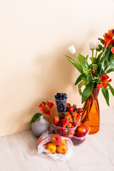 Wall Mural - floral and fruit composition with bouquet in vase and summer fruits on wooden surface on beige background