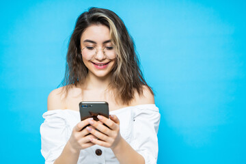 Wall Mural - Portrait of young smiling woman using mobile phone against blue background