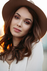 Beautiful positivity brunette woman in hat, white blouse, jeans walking at sunset in city, after shopping and beauty salon. Smiling fashionable girl stylish wearing posing at camera. Hipster look.