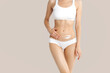 © Mirrorstudio - Slim young woman in underwear apply cream  to belly on beige background