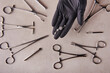 piercer master's hand in a medical black glove holds an earring. Around tool for piercing clamps