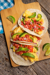 Breakfast egg tacos with flour tortilla and fresh sauce on wooden background