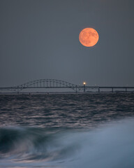 Wall Mural - Full moon rising in the sky above a silhouetted bridge and lighthouse. Fire Island, New York