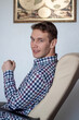 © Евгения Жигалкина - Caucasian  men  sits in the office chair and  looks into camera. Dressed into checkered shirt.