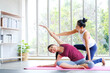 © Nipapun - Asian female yoga trainer  helping her trainees  stretching making tilts to the side before practice ,yoga at home,full length, Concept of healing body and spirit.Exercise at home